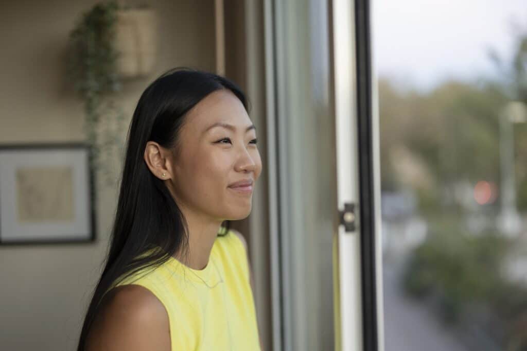 Happy asian woman looking through the window of her home